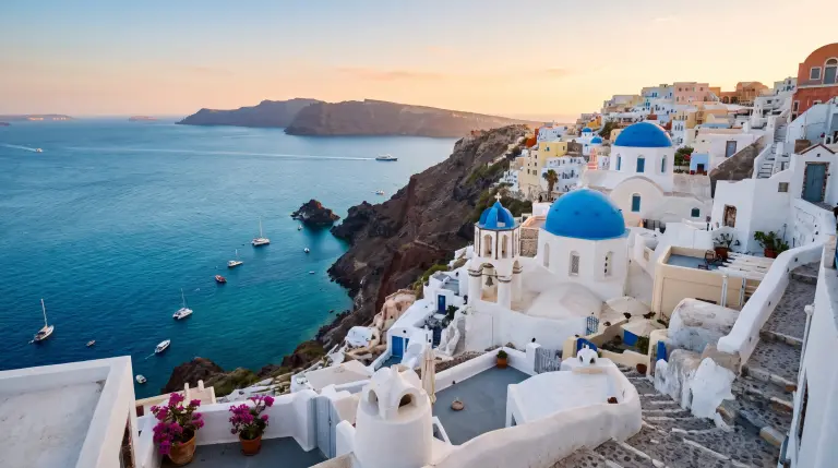The blue-domed white churches of Oia, Santorini, above the Aegean caldera at golden hour