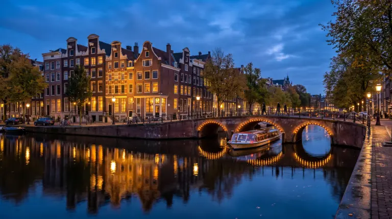 Amsterdam canals at blue hour, with gabled canal houses and a lit arched bridge